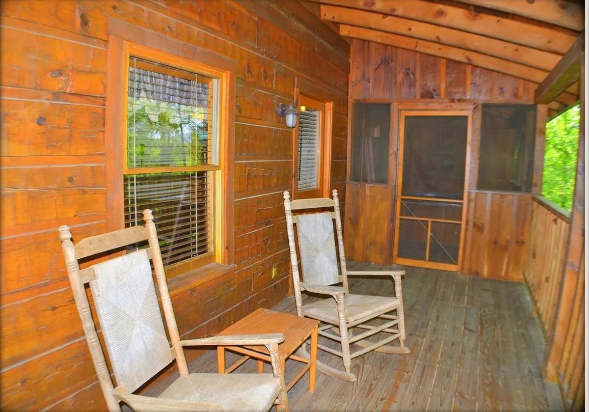 This image displays a pair of rocking chairs on a screened porch, with rich wooden walls and a screened door allowing fresh air and nature sounds to flow in. The mood is inviting, ideal for relaxing, reading, or simply enjoying the gentle ambiance of mountain life.