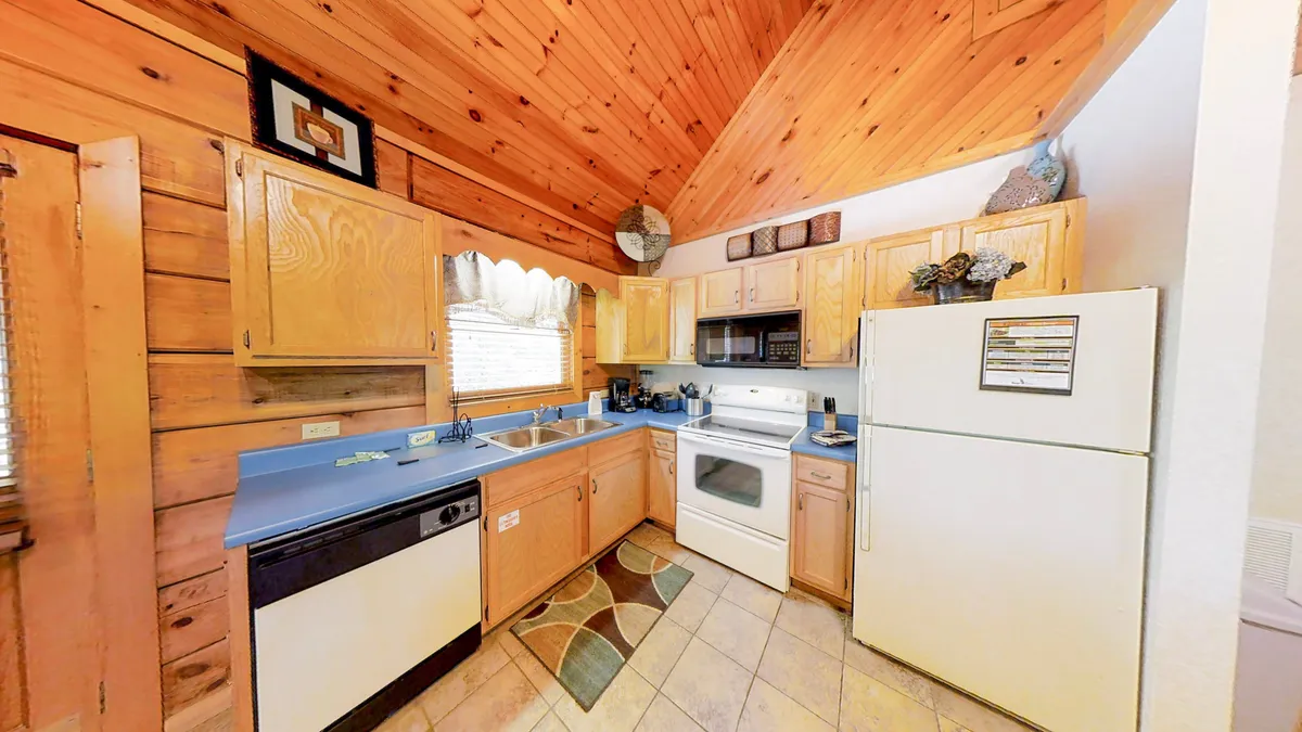 This image features a warm, inviting kitchen with wooden cabinetry, a blue countertop, and modern appliances. The setup clearly shows ample space for cooking and gathering, with practical amenities visible on the counters. The overall ambiance is homey and friendly, ideal for preparing meals and hosting loved ones.