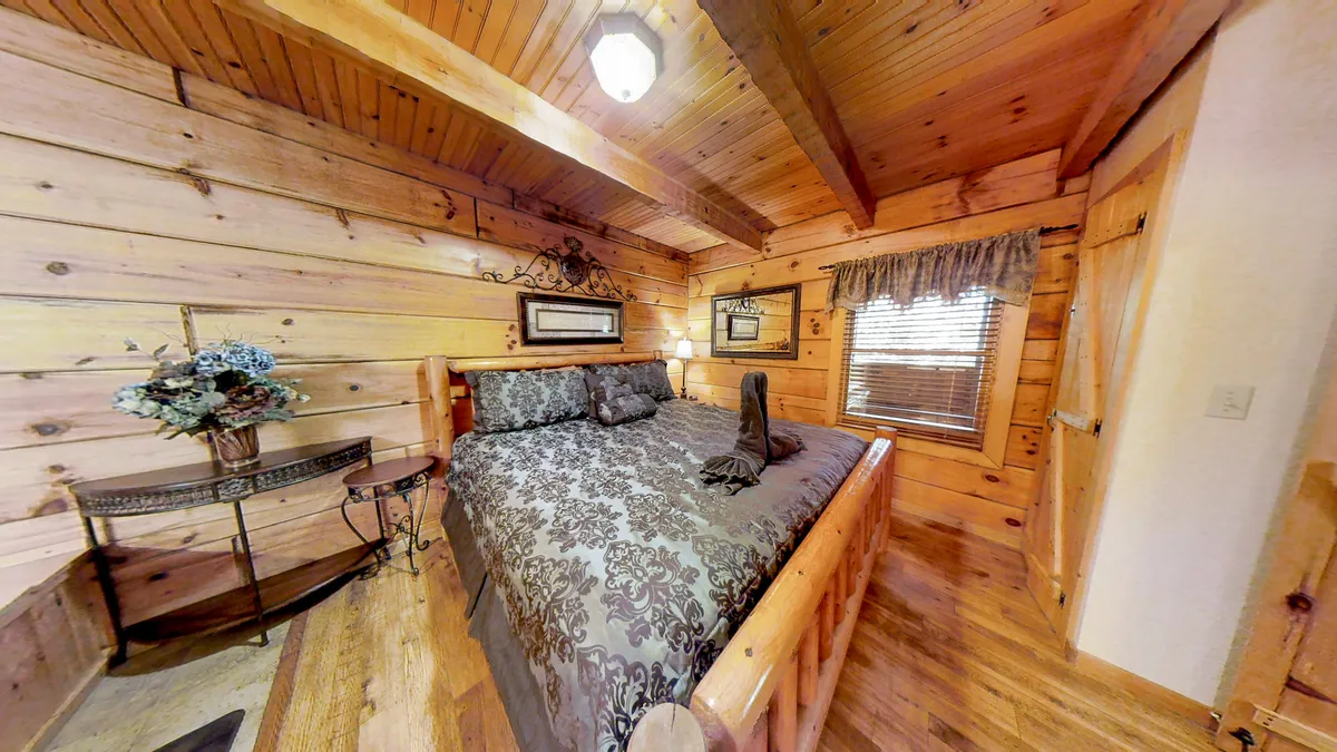 A cozy master bedroom featuring a wooden king bed frame, decorative bedding, wall art, and a nightstand with a floral arrangement. Sunlight gently filters into the room, highlighting the plush linens and inviting restful moments.