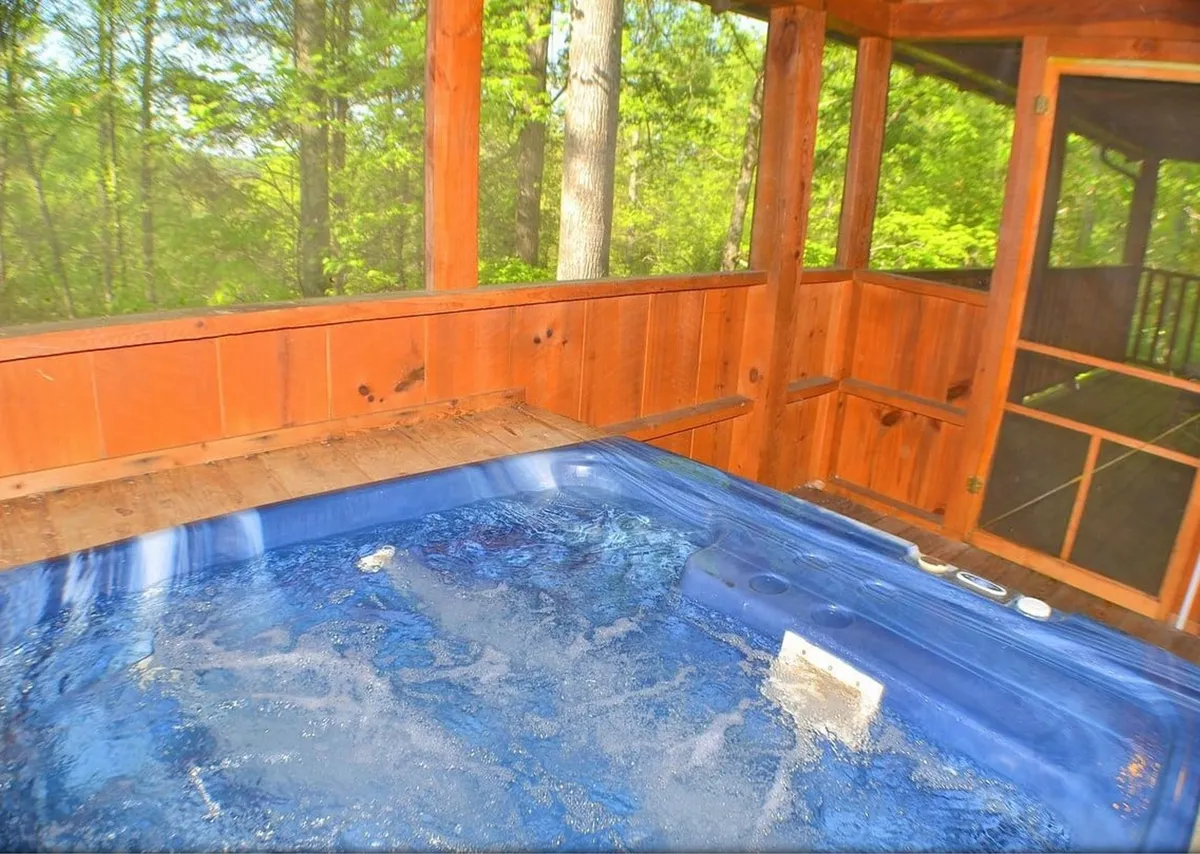 This image features a relaxing hot tub set against wooden walls, with lush greenery visible through the windows, creating an immersive connection to nature. The setting is serene, inviting guests to unwind and enjoy tranquil soaks while appreciating the natural surroundings.